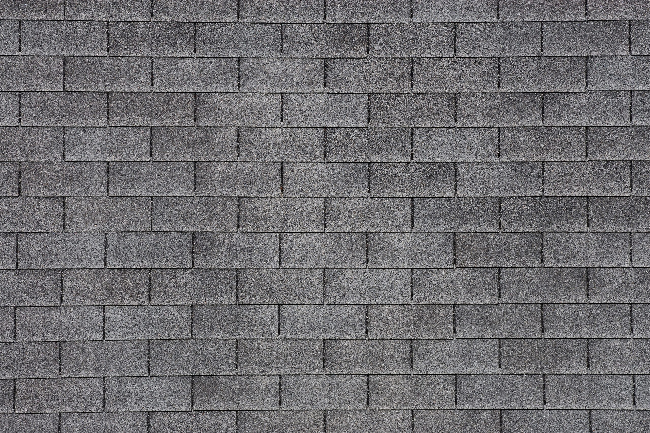 A close-up of a gray shingle roof with rectangular asphalt shingles arranged in a uniform pattern. The rough texture and even spacing create a consistent, grid-like appearance, reflecting the precision often required in storm roof repair.